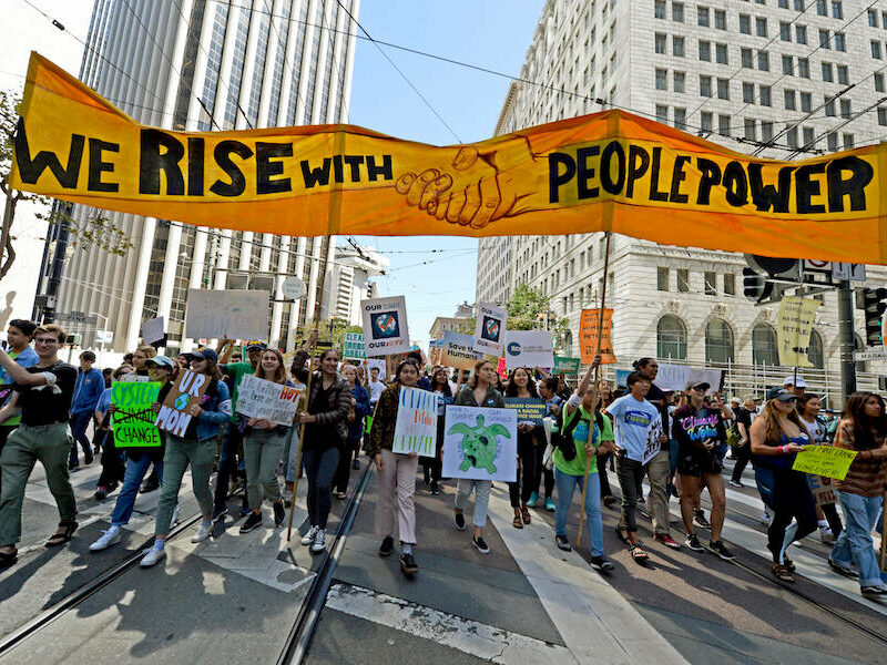 Marchers carry a banner displaying the words "We Rise With People Power"