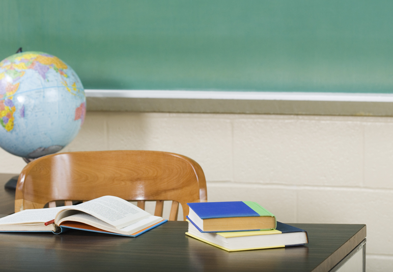 A globe and books sit on top of table in front of chalkboard