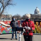 People stand in front of colorful signs, state Capitol Building in background