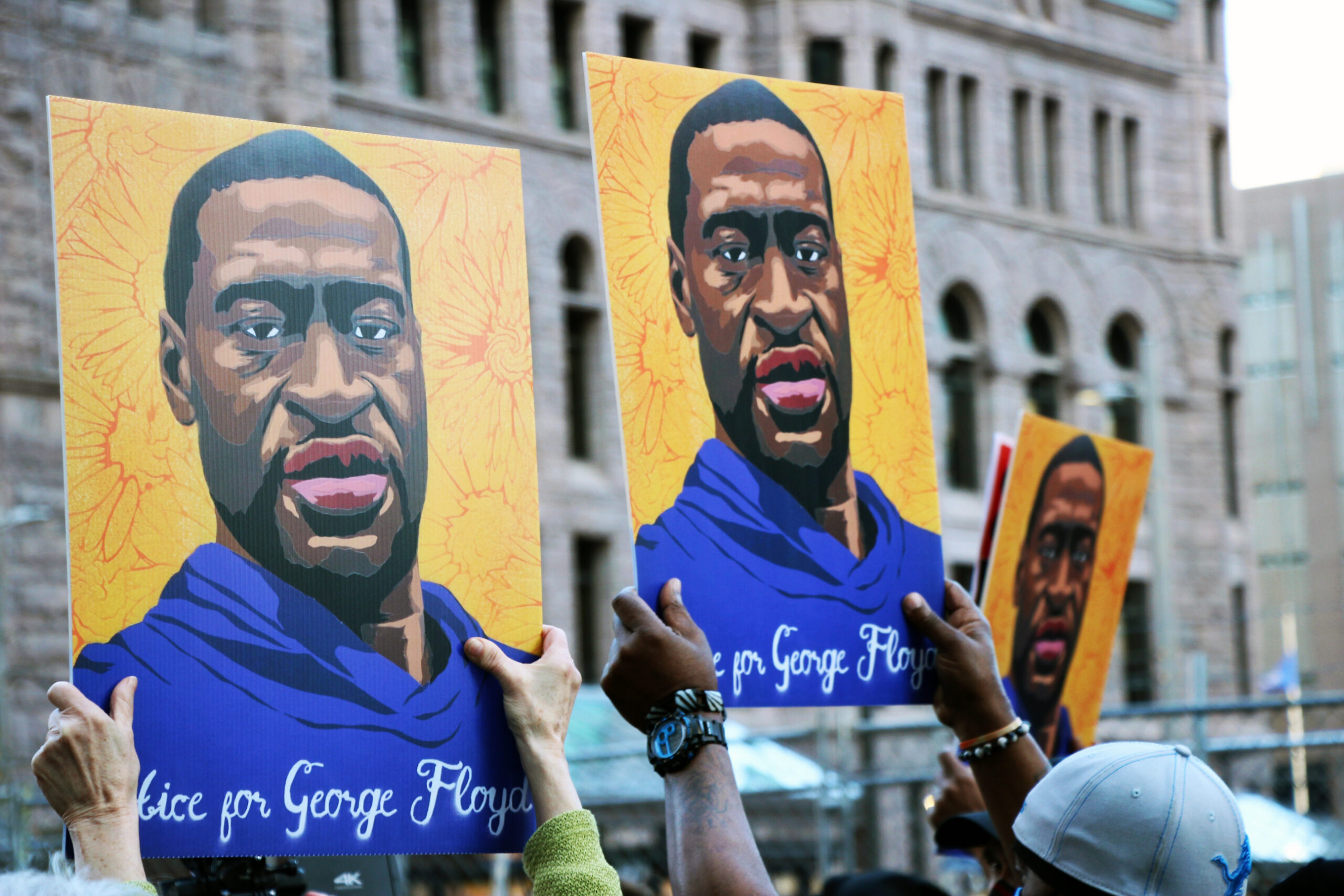 three yellow signs are held up that have George Floyd's face on them