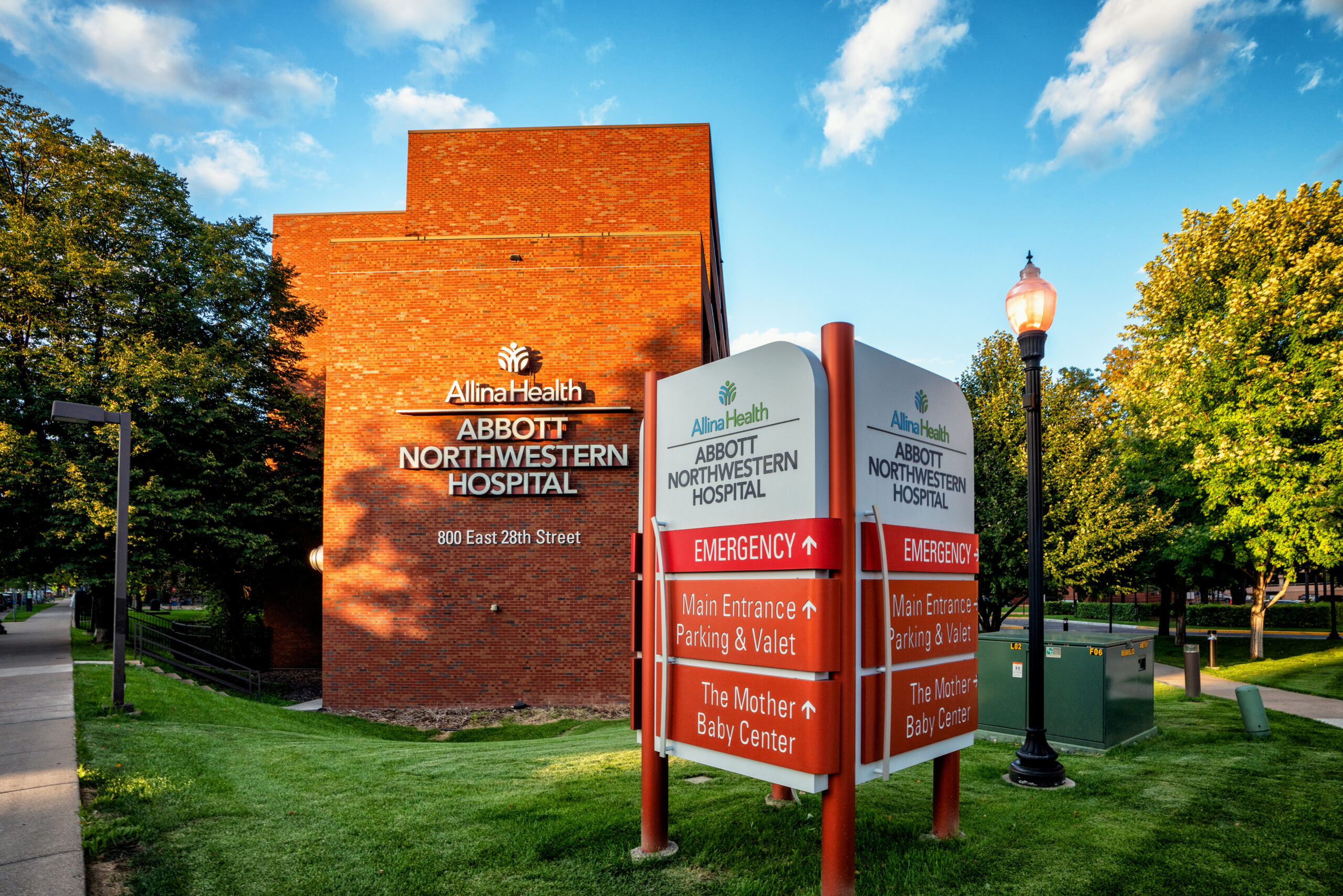 white and red sign with information about Allina Health building in front of brick building