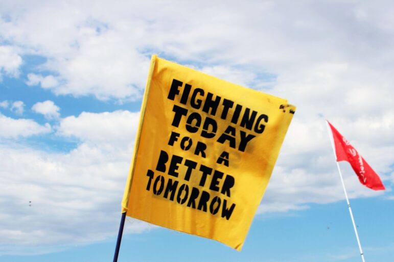 a square yellow flag with black text reads "fighting today for a better tomorrow"