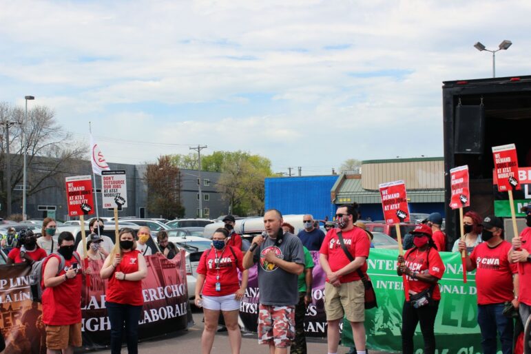 a white man speaks to the crowd in front of marchers in red shirts