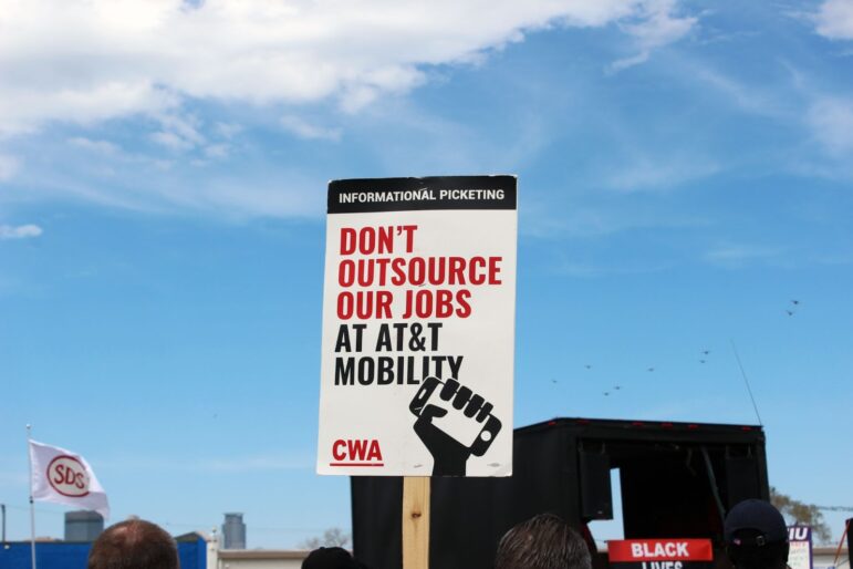 a sign reads "don't outsource our jobs at AT&T mobility" in red and black font