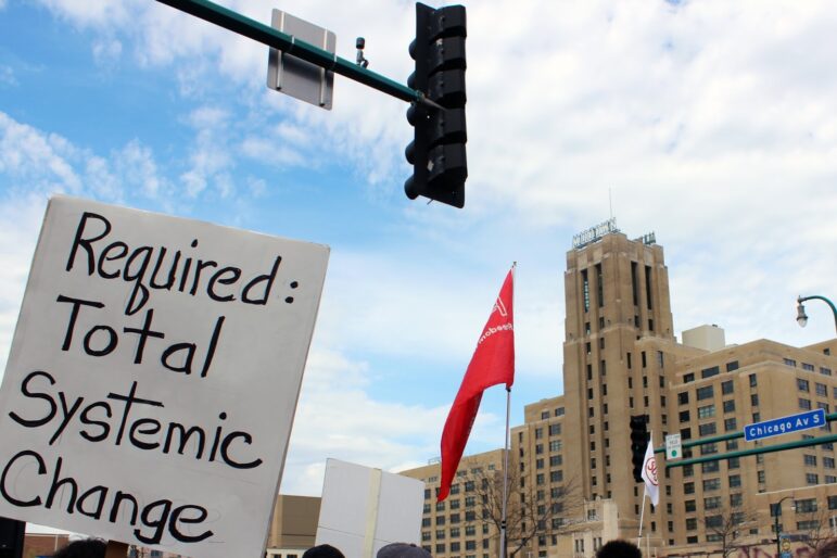 sign is held in front of intersection near midtown global market reading "required: total systemic change"