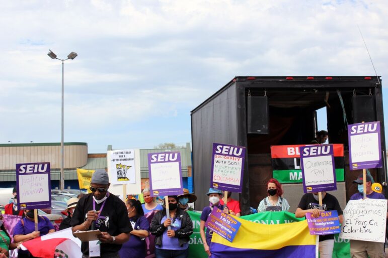 a black man reads from his phone in front of marchers holding signs from SEIU