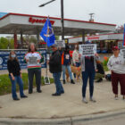 a group of people stand outside of Speedway gas station with signs reading "educators support refinery workers"