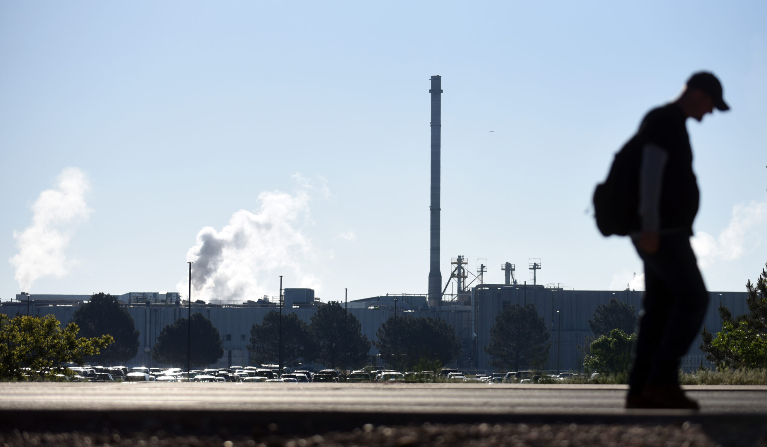 silhouette of a man in front of a blue sky and meatpacking facility towers with smoke pouring out