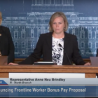 three blonde white women with black blazers stand behind a podium in front of a blue poster of the capitol building