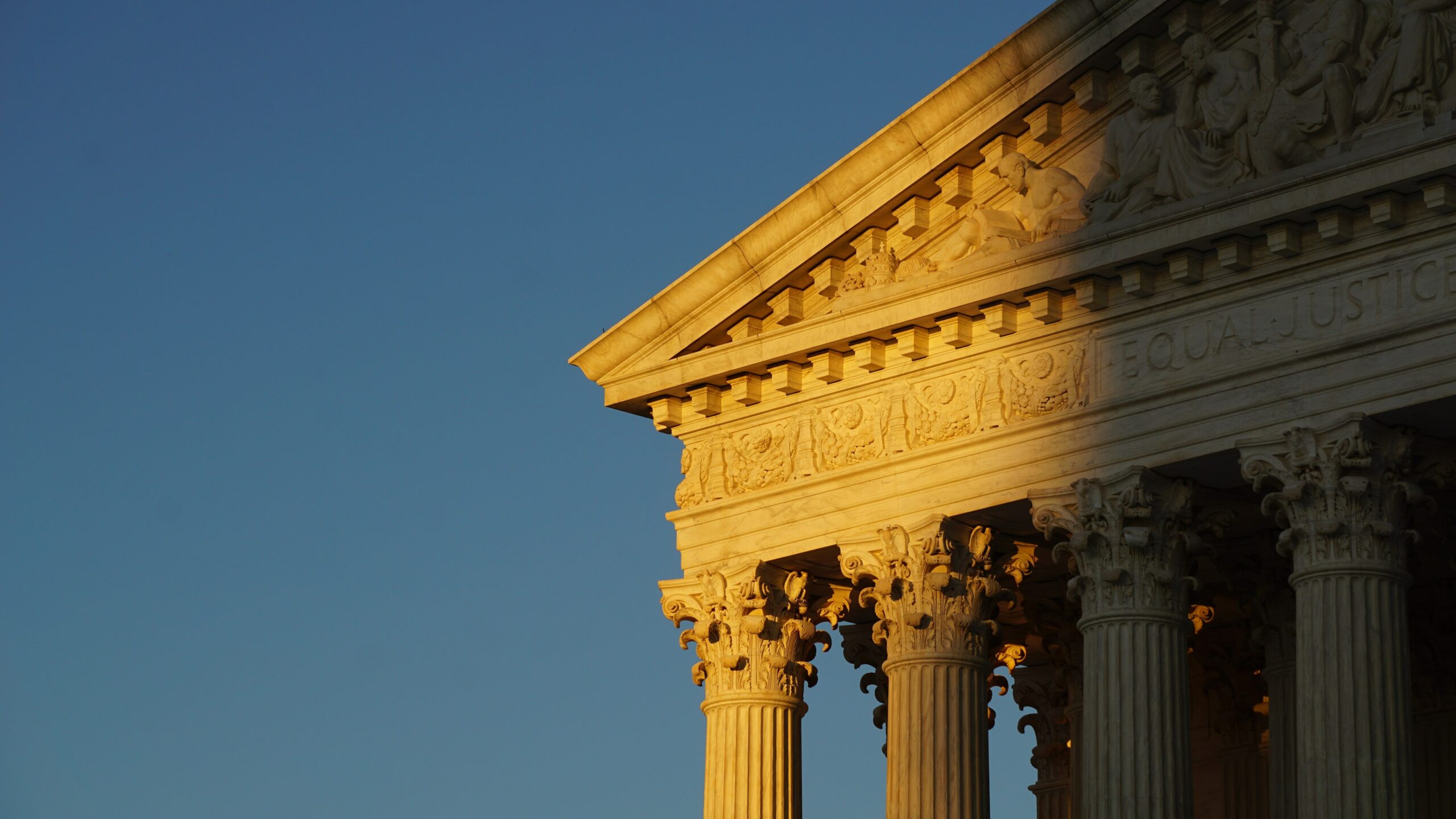 a corner of the supreme court building in golden light in front of a clear blue sky
