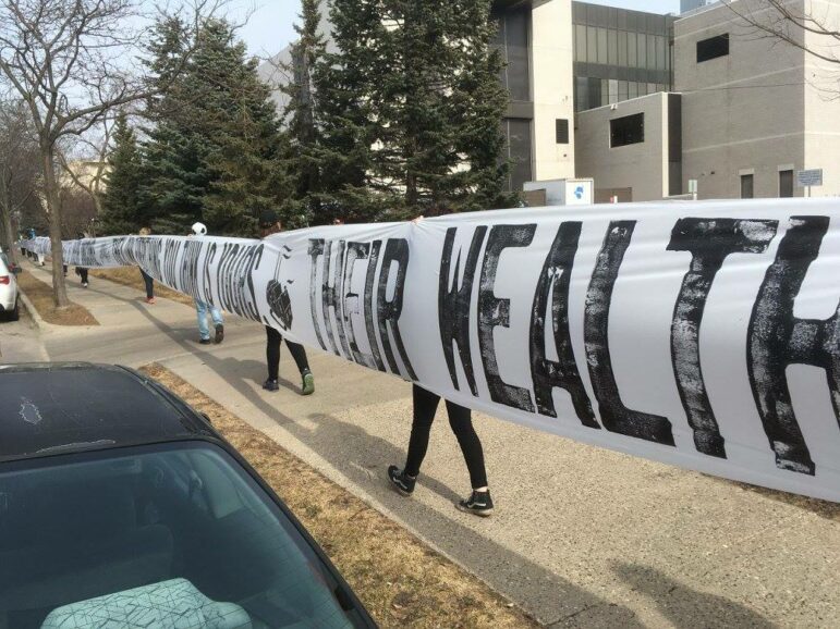 Students hold up a banner entitled "THEM" that reads, "Their wealth your misery" at the Minneapolis College of Art and Design