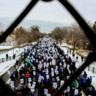 an aerial view of a protest march in the snow-lined streets, framed by a chain-link fence.