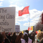 A crowd of protestors holding signs, one up close reads "The Working Class holds the Power"