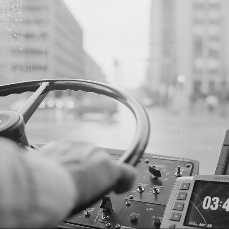 A photograph of Todd Eddy’s hands on the steering wheel as he drives the bus through downtown Minneapolis. Eddy drives the 6, 7, A Line, among other routes.