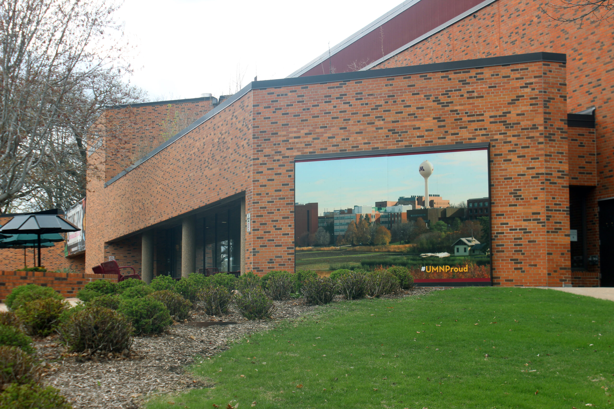 The brown brick exterior of the St. Paul campus food hall includes a photo of St. Paul campus behind green bushes and lawn