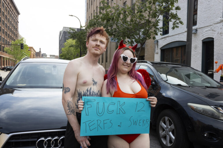 Two parade goers pose for a photo with a sign against police, transphobia, and anti sex worker bias.