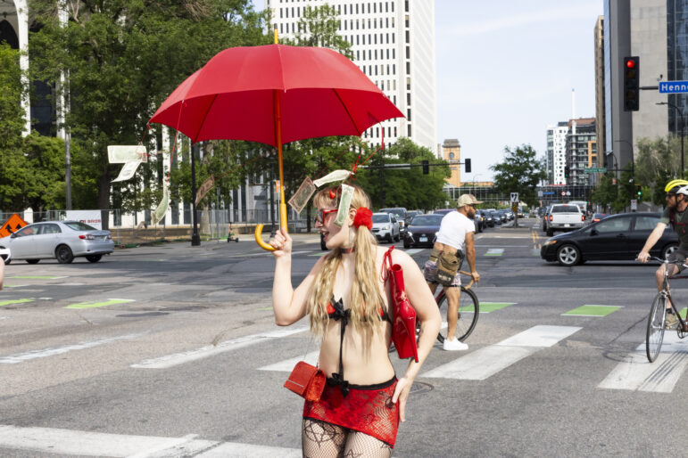 A marcher with a red umbrella with dollar bills hanging from its parasols. The red umbrella is a symbol for solidarity with sex workers.