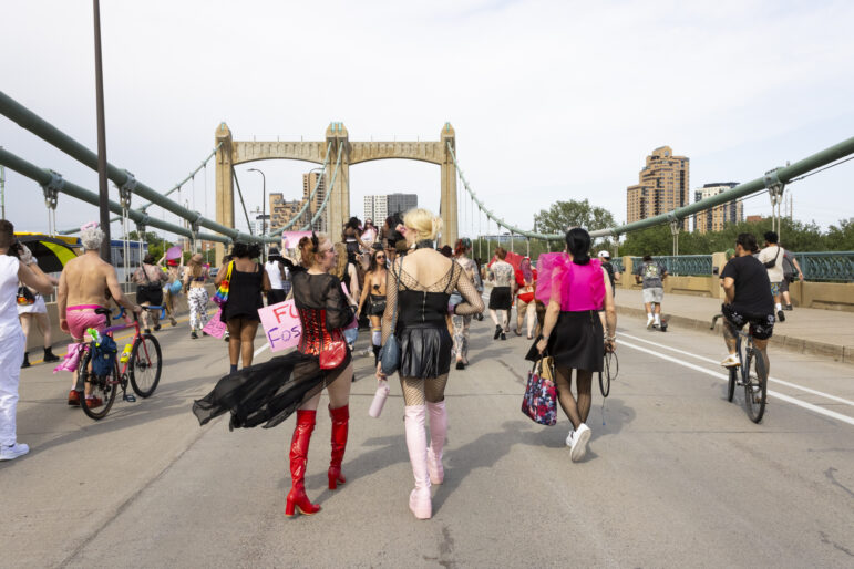 Two friends chat as the parade makes its way onto Hennepin Avenue Bridge.