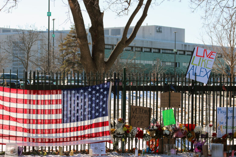 An american flag and posters are draped over the black iron fence outside of the Veterans Affairs hospital